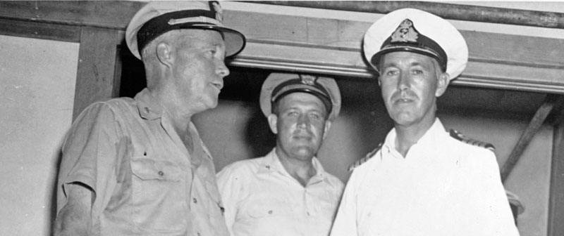 Officers of the U.S. and British Navies on board USS Lunga Point, 11 September 1945. They are (from left to right, front): Rear Admiral Ralph S. Riggs, USN, Commander Cruiser Division 12; Captain R.A.B. Edwards, RN, Commanding Officer, HMS Gambia; and Captain Joseph L. Kane, USN, Chief of Staff for Commander Escort Carrier Forces, Pacific. Collection of Vice Admiral Calvin T. Durgin. Donated by his daughter, Mrs. Phyllis Durgin Sherrill, 1969. Official U.S. Navy Photograph, from the collections of the Naval History and Heritage Command NH 69409.