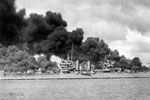 U.S. Navy light cruiser USS Phoenix (CL-46) steams down the channel off Ford Island's "Battleship Row," past the sunken and burning USS West Virginia (BB-48), at left, and USS Arizona (BB-39), at right, 7 December 1941. U.S. National Archives 12008993