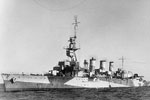 HMS Adelaide, port bow view. She is shown in her third armament configuration, armed with seven 6 inch and two 4 inch AA guns. Two 6 inch guns have been replaced in the waist by depth charge throwers; one of the guns has been remounted on the centreline aft, replacing a 4 inch AA gun. 20 mm Oerlikon AA guns are mounted port and starboard in the bridge wings, amidships and on the searchlight platform. The cruiser has been fitted with air search radar on her foremast, gunnery control radar on her main armament director and surface search radar on a platform forward of the fore funnel. Australian War Memorial 300081
