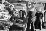 HMS Jamaica, sister ship to HMS Gambia. The interior of a 6" triple Mark XXIII mounting. Note the crew wearing anti flash gear. From this angle you can see the centre and right 6" Mark XXIII guns of the three contained within this turret. The crew member in the foreground has over his shoulder a 30 pound cordite propellant charge. Note a further charge is emerging from the cordite hoist in the floor. It is still in its protective case. Photo: Lt. H. A. Mason. Imperial War Museums A 16320